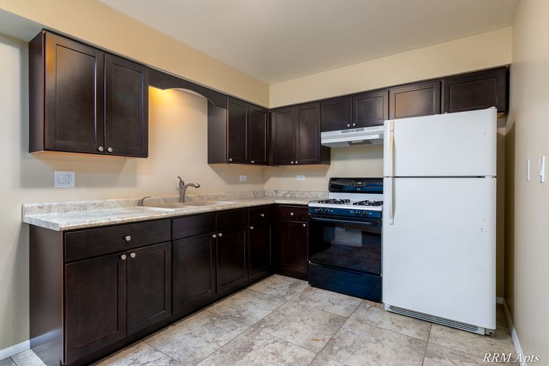Kitchen with dark brown cabinets, black stove, white refrigerator and granite-look counter, Pistakee Road apartment 1C