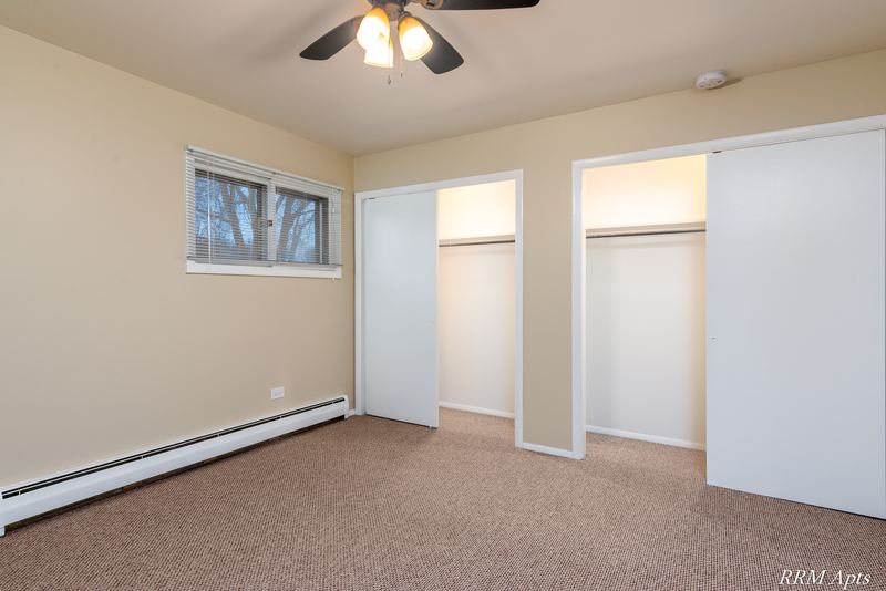 Bedroom with beige carpet, ceiling fan, window and two open closets with shelves, Pistakee Road apartment 1C