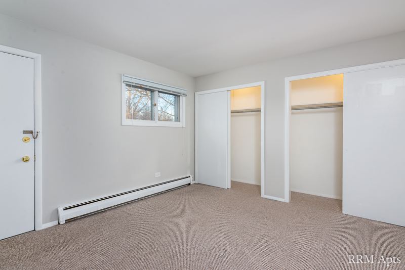 Carpeted bedroom with window and two open closets, Pistakee Road apartment 1D
