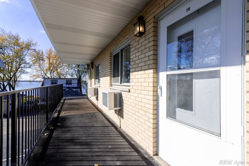 Building exterior with covered walkway, black metal railing, brick wall and windows, Pistakee Road apartment 2B