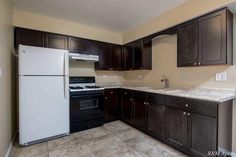 Kitchen with dark brown cabinets, white refrigerator, black stove and granite-look counters, Pistakee Road apartment 2B
