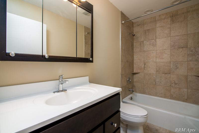 Bathroom with dark vanity, mirrored cabinet, toilet and tub with tan tile surround, Pistakee Road apartment 2B