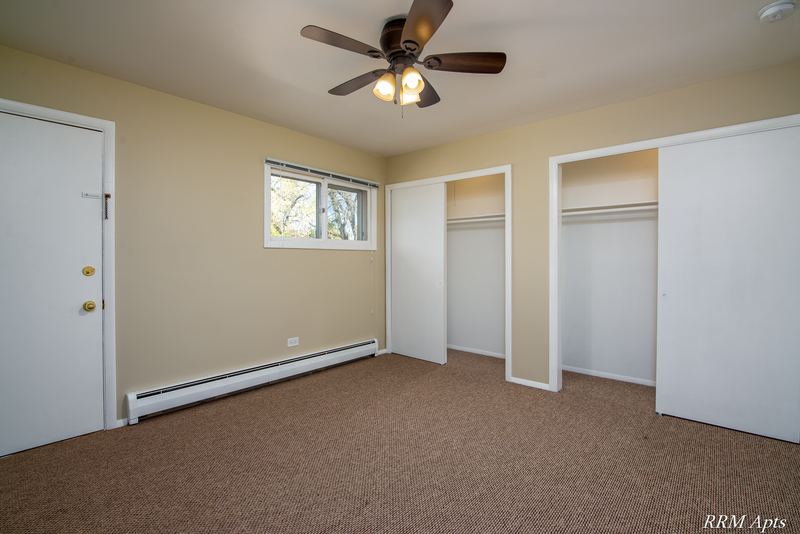 Bedroom with beige carpet, ceiling fan, window, two open closets and a wood door, Pistakee Road apartment 2B