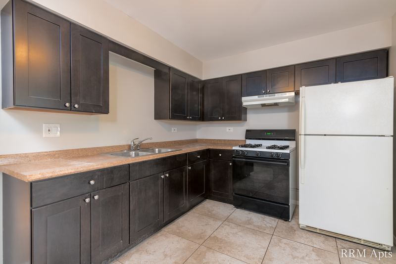 Kitchen with dark brown cabinets, black stove, white refrigerator and tile floor, Pistakee Road apartment 2C