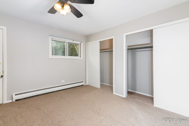 Bedroom with beige carpet, ceiling fan, window and two open closets, baseboard heater, Pistakee Road apartment 2C