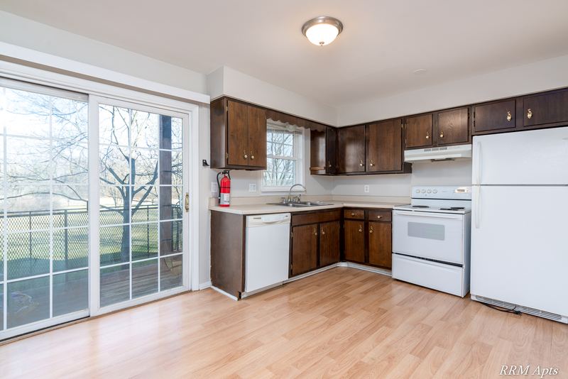 Kitchen with dark brown cabinets, white appliances, wood floor and sliding glass patio door, Prairie Ridge apartment 9716 1B