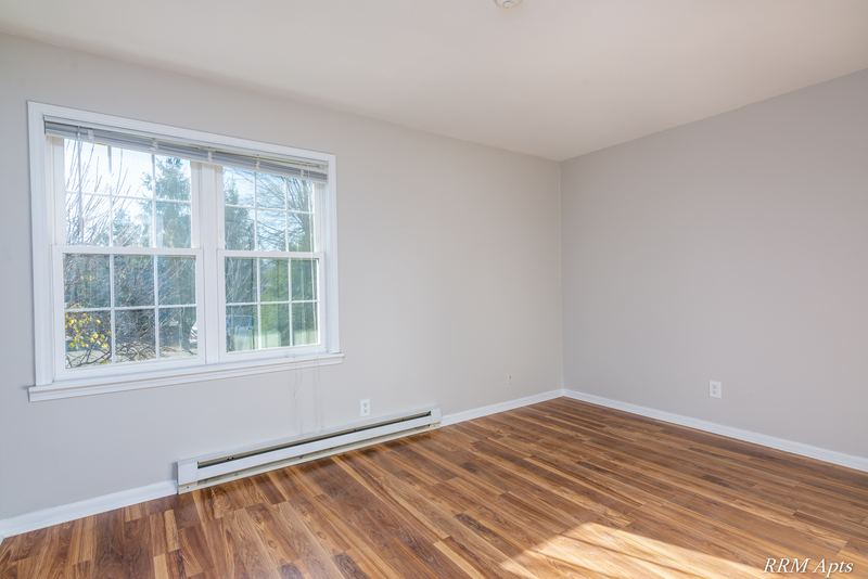 Empty room with wood floor, window onto trees and a baseboard heater, Prairie Ridge apartment 9716 1B