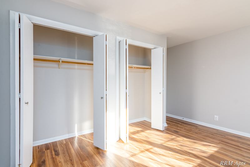 Bedroom with wood floor and two open closets with white folding doors and rods, Prairie Ridge apartment 9716 1B