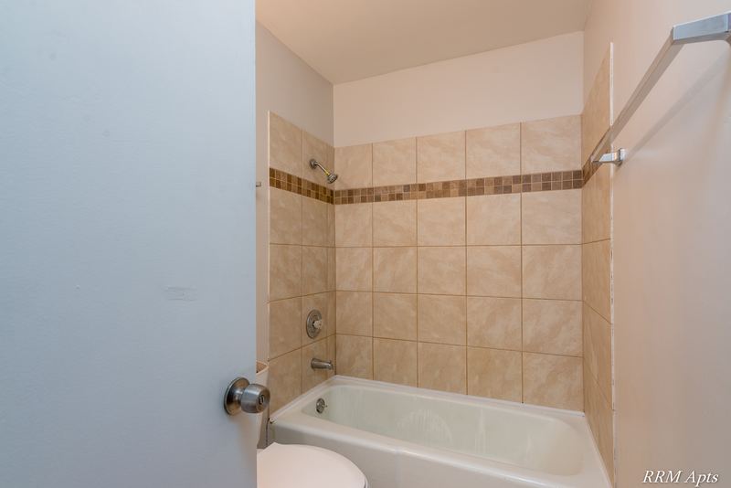 Bathroom with white tub and beige tile surround with a mosaic accent strip, Prairie Ridge apartment 9716 1B