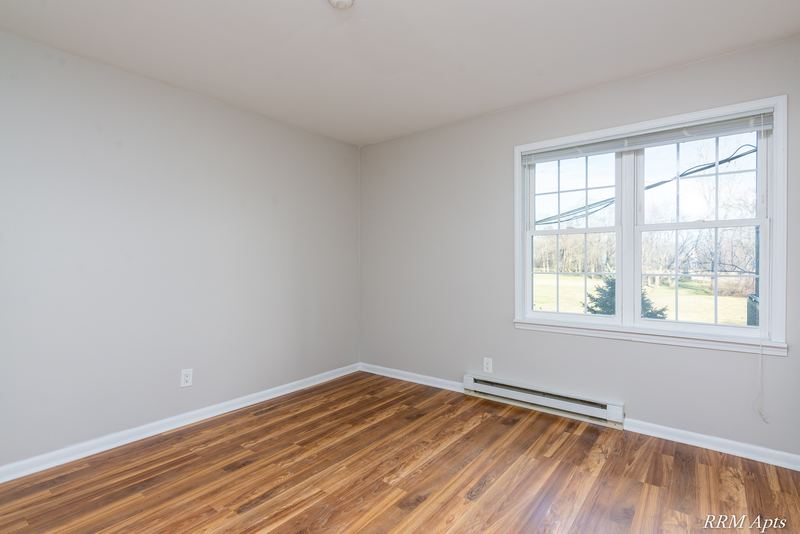 Empty room with wood floor, window looking out to a field and a baseboard heater, Prairie Ridge apartment 9716 1B
