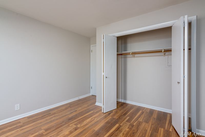 Bedroom with wood floor, open closet with folding doors and rod, and a doorway, Prairie Ridge apartment 9716 1B