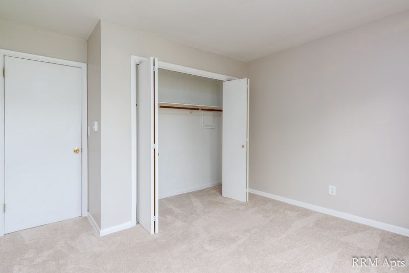 Bedroom with beige carpet, white door and an open closet with folding doors and rod, Prairie Ridge apartment 9716 2B