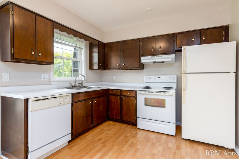 Kitchen with dark brown cabinets, white refrigerator, stove and dishwasher, wood floor, Prairie Ridge apartment 9716 2B