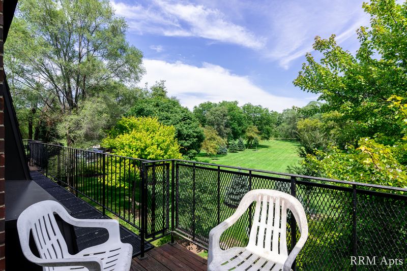 Balcony with two white chairs, black railing and a view of trees and lawn, Prairie Ridge apartment 9716 2B