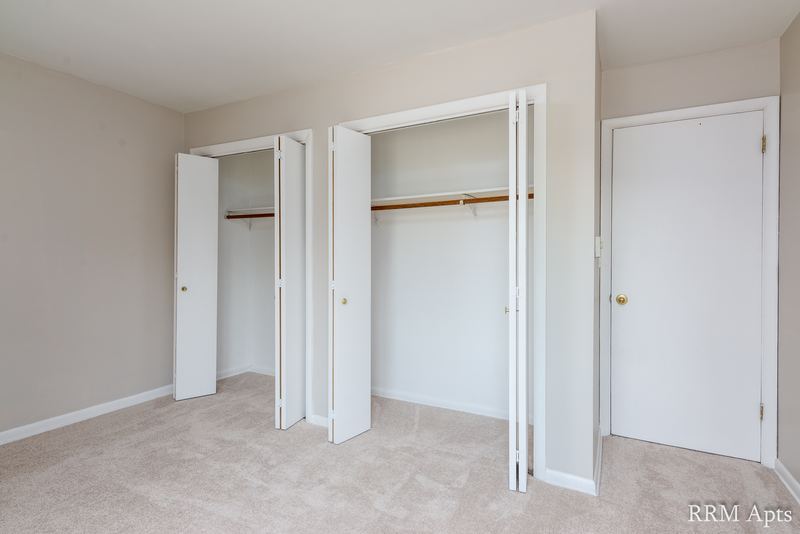 Bedroom with beige carpet, two open closets with folding doors and a white door, Prairie Ridge apartment 9716 2B
