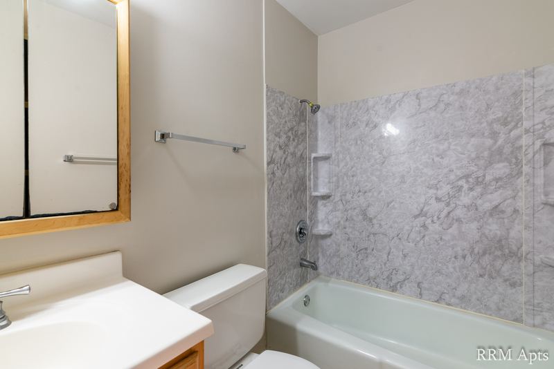 Bathroom with tub with gray marble-look surround, toilet and vanity with mirror, Prairie Ridge apartment 9716 2B
