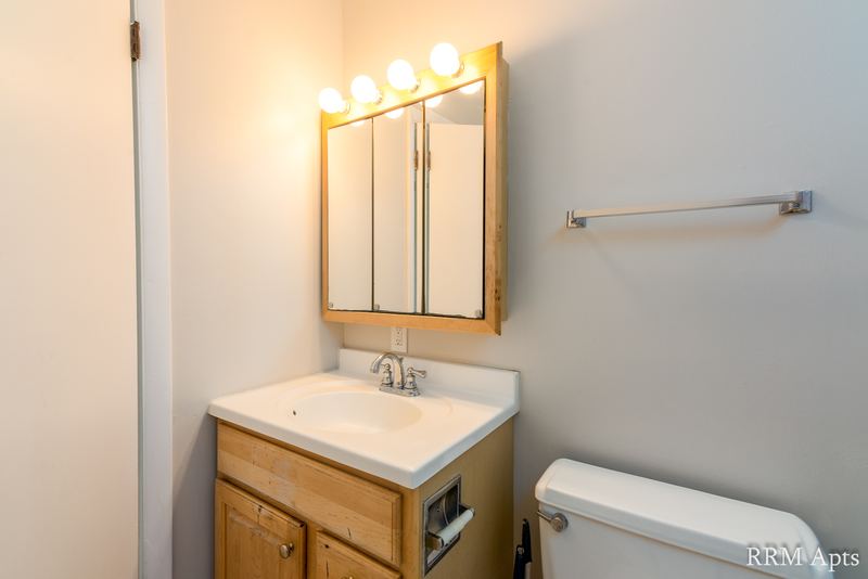 Bathroom with wood vanity, mirrored cabinet with light bar and toilet, Prairie Ridge apartment 9716 2B