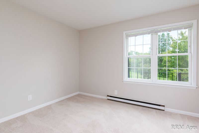Empty room with beige carpet, window onto trees and a baseboard heater, Prairie Ridge apartment 9716 2B