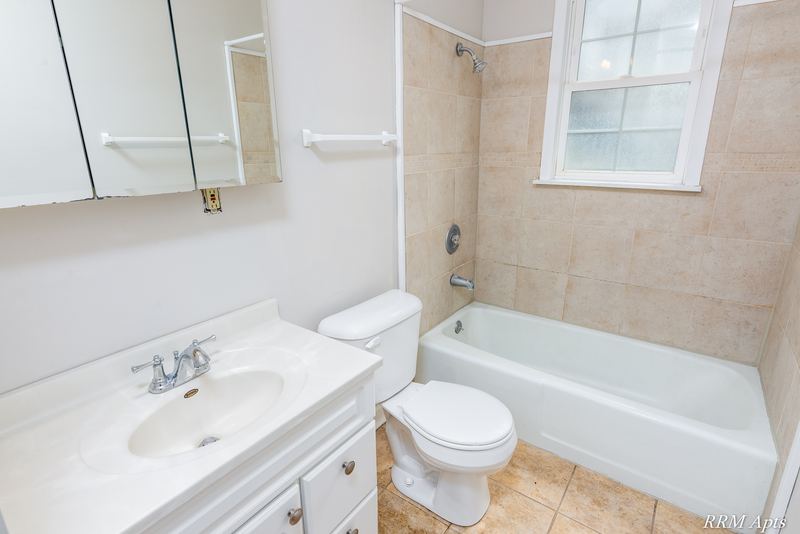 Bathroom with white vanity, mirrored cabinet, toilet and tub with beige tile and window, Prairie Ridge apartment 9716 GA
