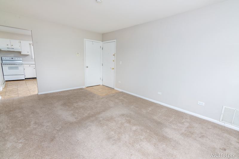 Living room with beige carpet, a door and an opening to a kitchen with white stove, Prairie Ridge apartment 9716 GA