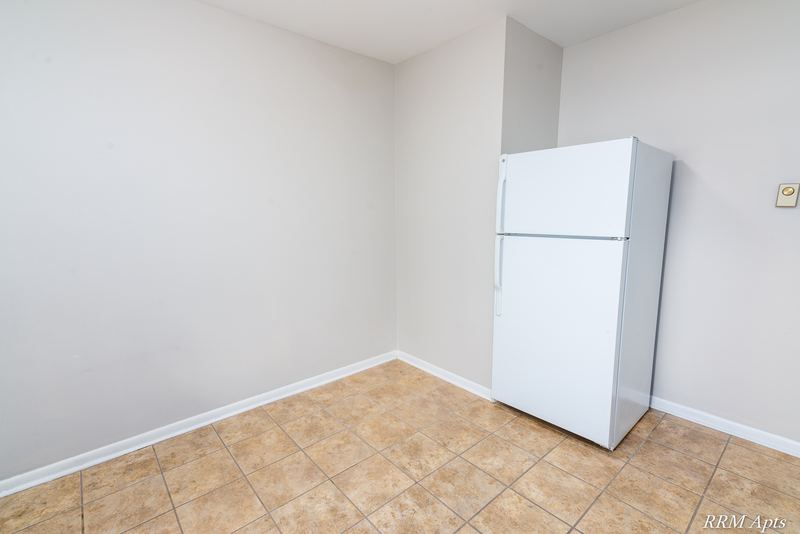 Kitchen corner with white refrigerator, bare walls and tan tile floor, Prairie Ridge apartment 9716 GA