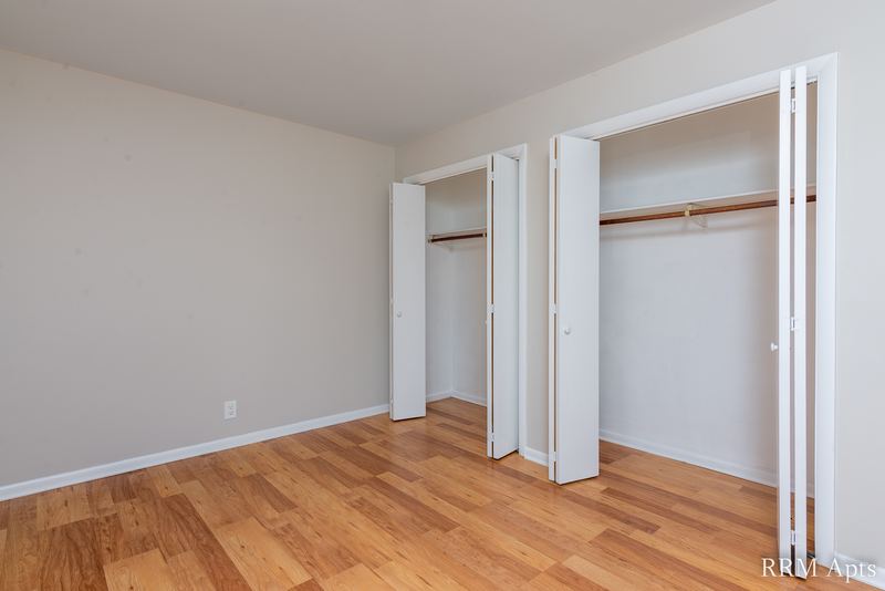 Bedroom with wood floor, two open closets with folding doors and a doorway, Prairie Ridge apartment 9718-1D