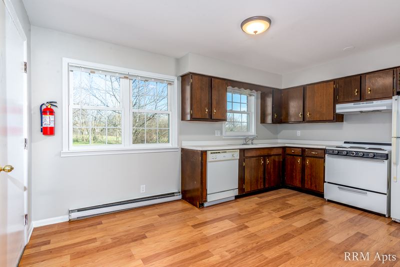 Kitchen with dark wood cabinets, white dishwasher and stove, window and wood floor, Prairie Ridge apartment 9718-1D
