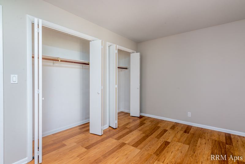 Bedroom with wood floor and two open closets with folding doors and rods, Prairie Ridge apartment 9718-1D