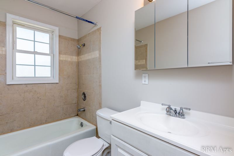 Bathroom with tub with beige tile surround, window, toilet and white vanity with mirror, Prairie Ridge apartment 9718-1D