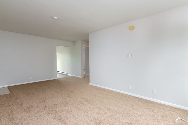 Living room with beige carpet, bare walls and an opening to the hall and kitchen, Prairie Ridge apartment 9718 2C