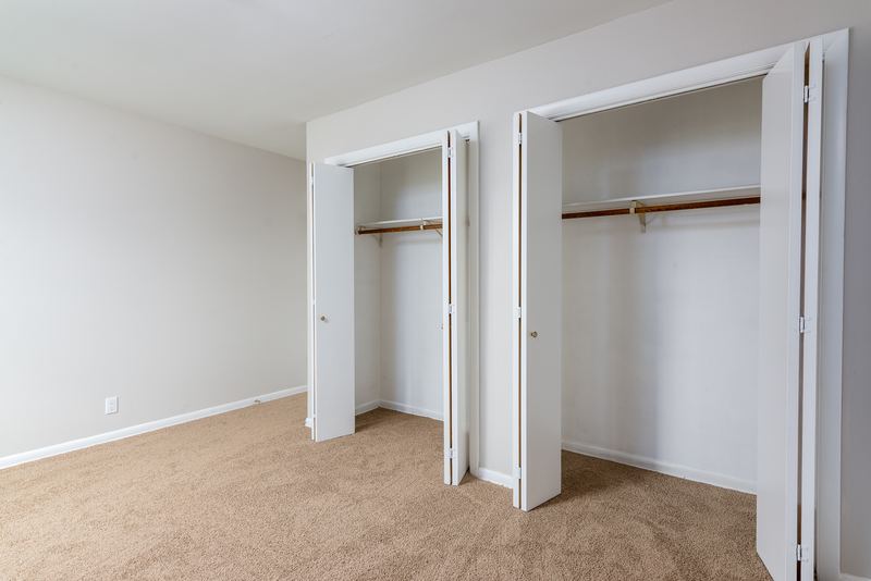 Bedroom with beige carpet and two open closets with folding doors and rods, Prairie Ridge apartment 9718 2C