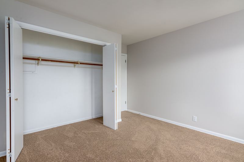 Bedroom with beige carpet, open closet with folding doors and rod, and a doorway, Prairie Ridge apartment 9718 2C
