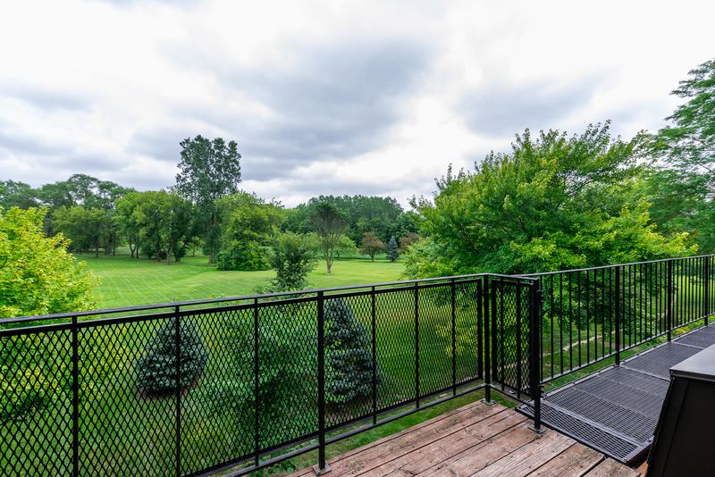 Balcony with black metal railing overlooking a lawn and trees under a cloudy sky, Prairie Ridge apartment 9718 2C