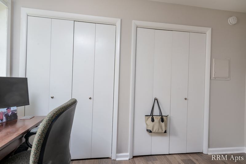Bedroom with white folding closet doors, white door, desk chair and a monitor, Prairie Ridge apartment 9718 GC