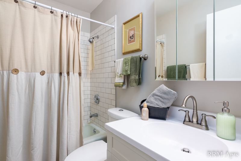 Bathroom with shower curtain, white tile tub surround, toilet and mirrored cabinet, Prairie Ridge apartment 9718 GC