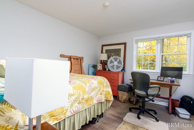 Bedroom with bed, desk and office chair, fan and window onto autumn trees, Prairie Ridge apartment 9718 GC