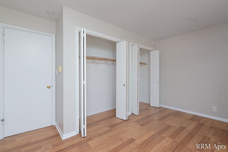 Bedroom with wood floor, white door and two open closets with folding doors, Prairie Ridge apartment 9806 1A