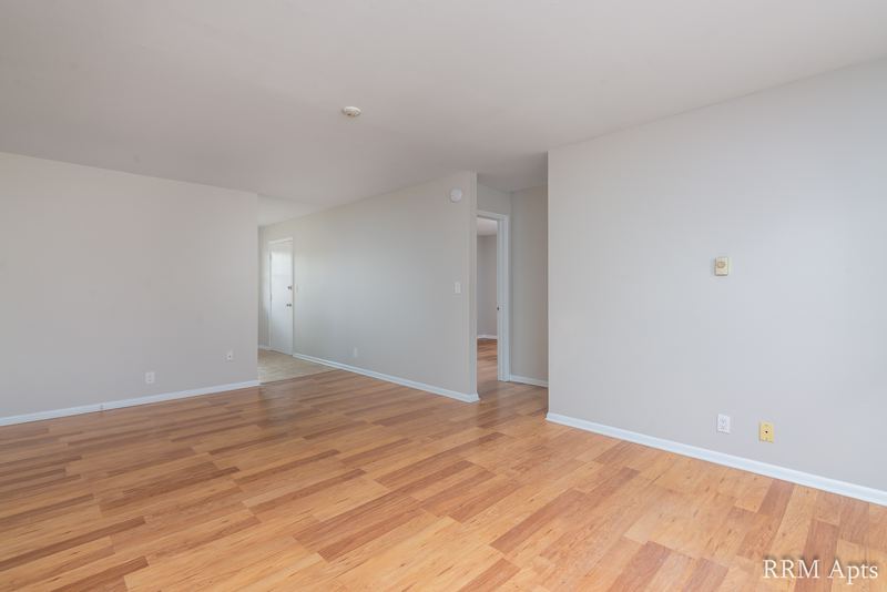 Living room with wood floor, bare walls and a hallway opening, Prairie Ridge apartment 9806 1A