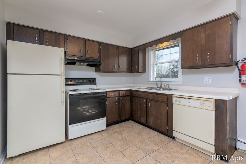 Kitchen with dark wood cabinets, white refrigerator, stove and dishwasher, tile floor, Prairie Ridge apartment 9806 1A