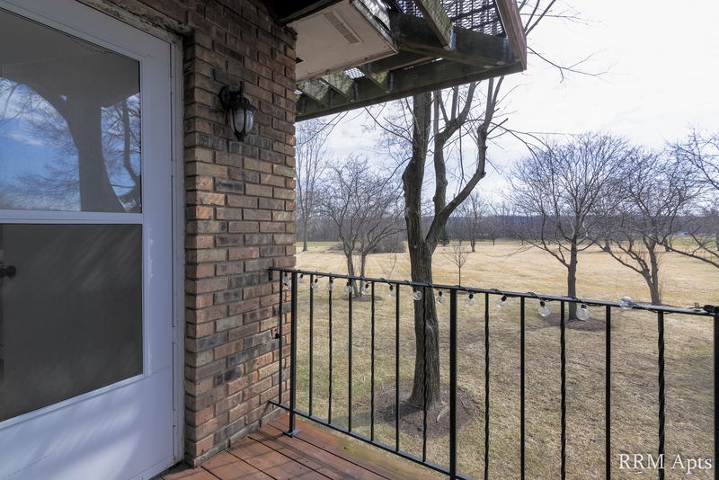 Entry with glass storm door, brick wall, black railing and view of bare trees, Prairie Ridge apartment 9806 1A