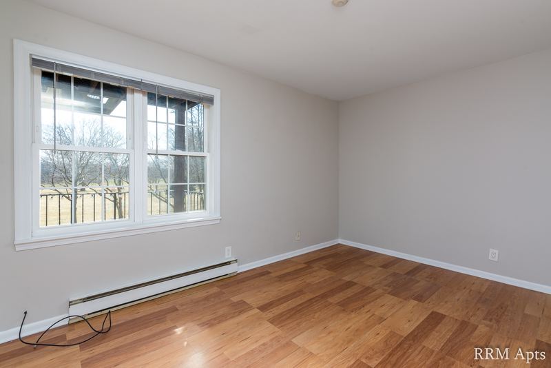 Empty room with wood floor, double window onto bare trees and a baseboard heater, Prairie Ridge apartment 9806 1A