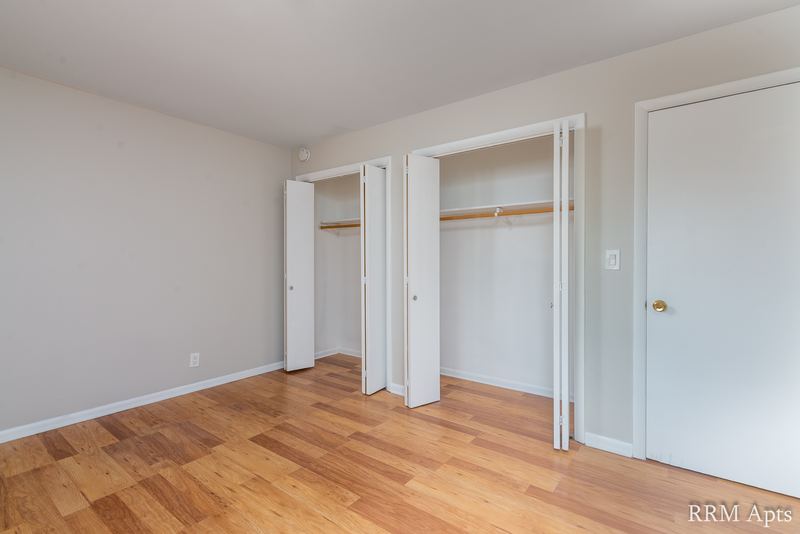 Bedroom with wood floor, two open closets with folding doors and a white door, Prairie Ridge apartment 9806 1A