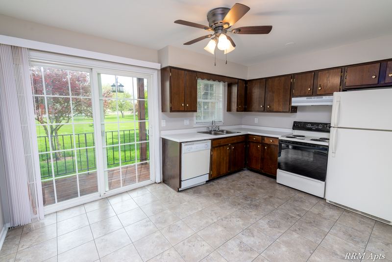Kitchen with dark wood cabinets, white appliances, ceiling fan and a sliding glass door, Prairie Ridge apartment 9806-1B
