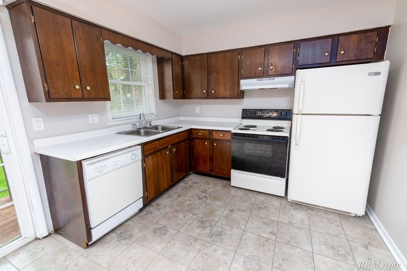 Kitchen with dark wood cabinets, white dishwasher, stove and refrigerator, tile floor, Prairie Ridge apartment 9806-1B