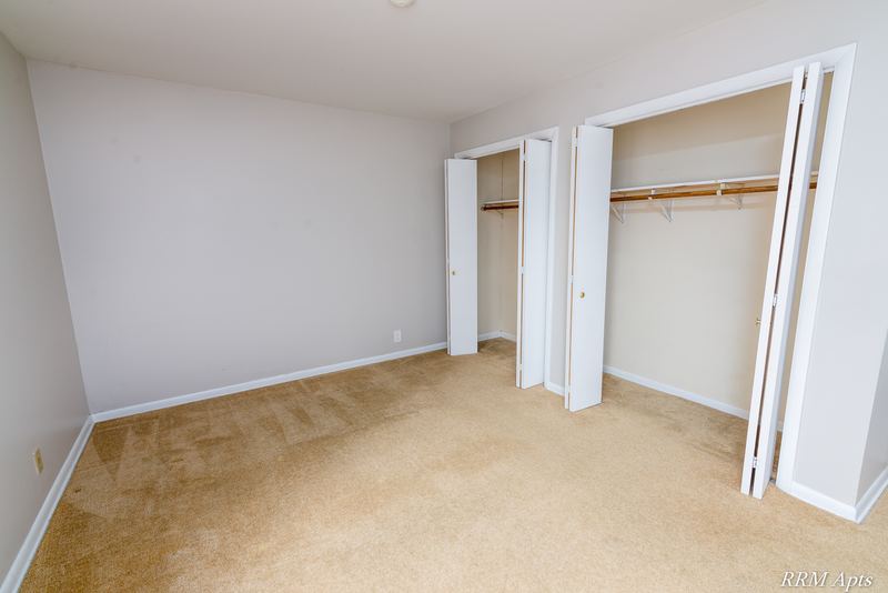 Bedroom with beige carpet and two open closets with folding doors and rods, Prairie Ridge apartment 9806-1B
