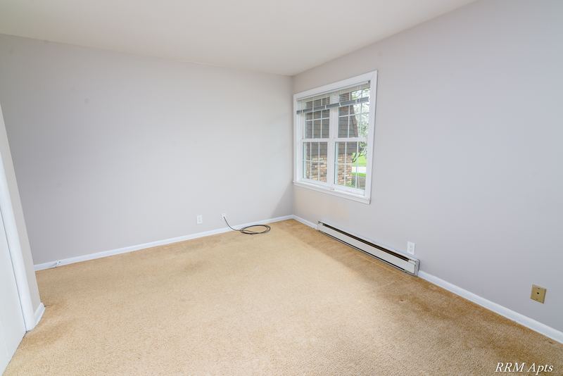 Empty room with beige carpet, window with trees outside and a baseboard heater, Prairie Ridge apartment 9806-1B