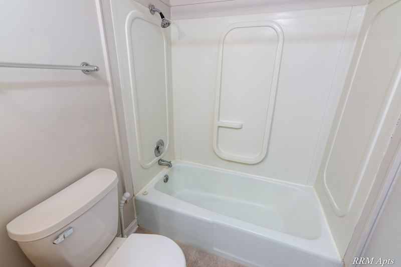 Bathroom with white one-piece tub and shower surround, toilet and grab bar, Prairie Ridge apartment 9806-1B