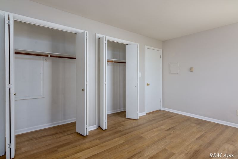 Bedroom with wood floor, white door and two open closets with rods, Prairie Ridge apartment 9806 GA