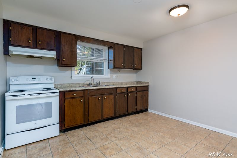 Kitchen with dark wood cabinets, white electric stove, window and tan tile floor, Prairie Ridge apartment 9806 GA