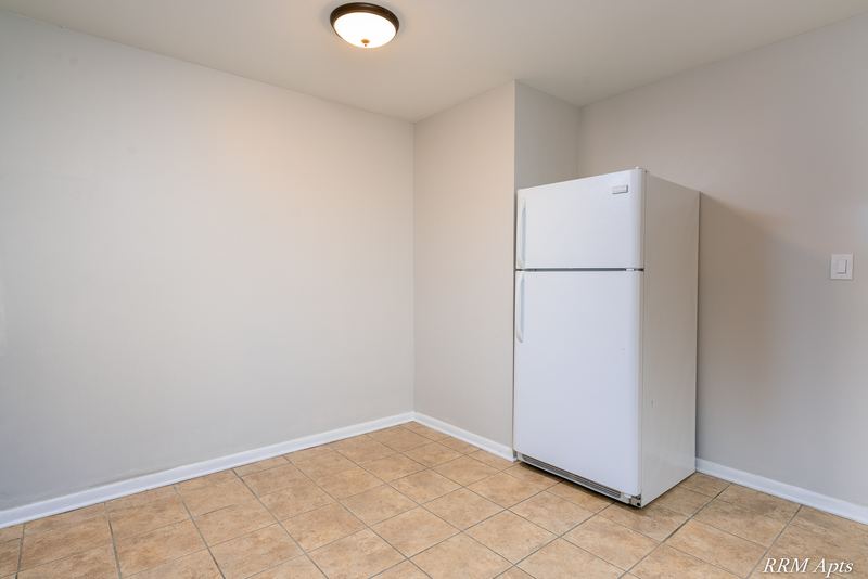 Kitchen corner with a white refrigerator and tan tile floor under a ceiling light, Prairie Ridge apartment 9806 GA
